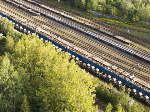Aerial view of freight trains carrying industrial cargo on parallel railway tracks bordered by lush green trees in Poland.