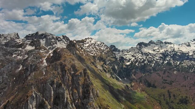 Aerial view of amazing rocky mountains in snow and green valley, Prokletie park, Montenegro and Albania, panorama 4k
