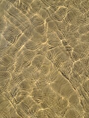 Top down close up background of golden sun caustics and light water ripples on a shallow sandy sea floor in Jurmala. © Irina