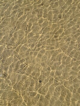 Top down close up background of golden sun caustics and light water ripples on a shallow sandy sea floor in Jurmala.