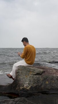 Man Sitting on a Helsinki Beach Looking at His Phone on a Cloudy Day