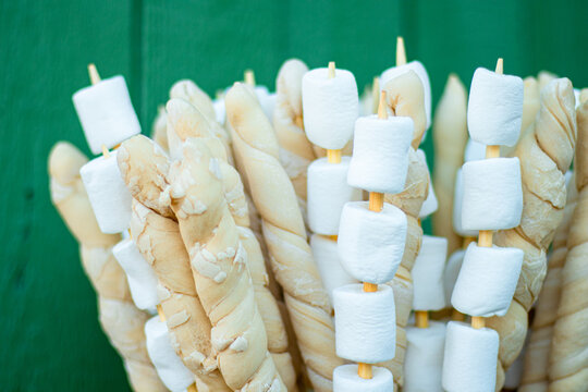 Skewers with marshmallows and dough twists arranged together against a green wooden background, ideal for outdoor cooking or camping adventures