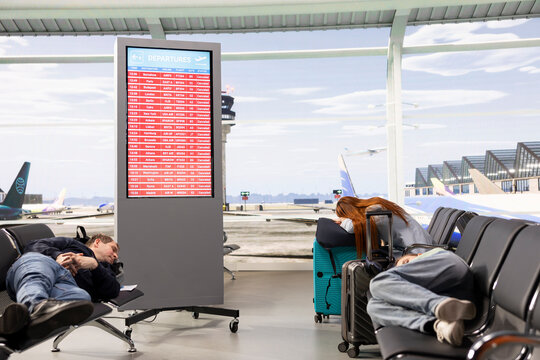 Unhappy travelers sleep in an airport waiting area after flight cancellations ground departures, while red alerts signal disruption and airline crisis.