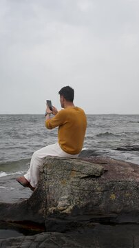 Man Sitting on the Beach Taking Photos With His Smartphone