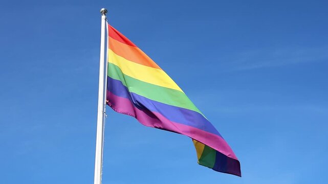 Rainbow pride flag waving in slow motion against a blue sky
