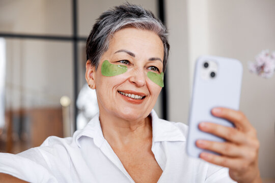 Senior woman using eye patches taking selfie with smartphone