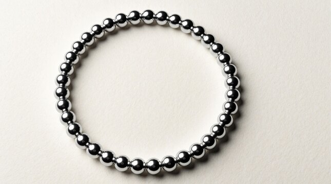 Silver bead bracelet forms a perfect circle shape on white surface. Uniform shiny metal beads suggest concepts of endless cycle renewal and connection.