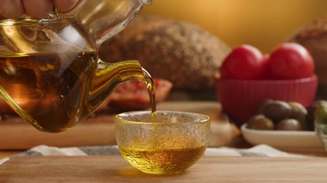 Chef pouring fresh olive oil over Mediterranean table with olives and bread