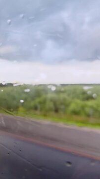 Rain-soaked countryside through a car window on a cloudy day