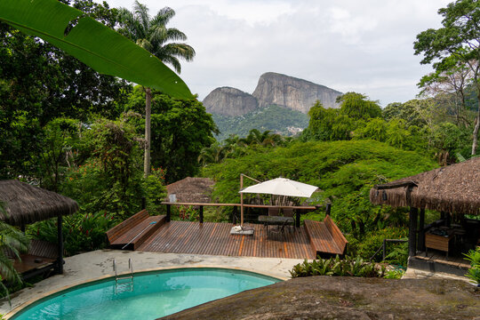 View of a swimming pool and wooden deck surrounded by lush tropical vegetation with the mountains of Tijuca National Park in the background in Rio de Janeiro, Rio de Janeiro, Brazil.