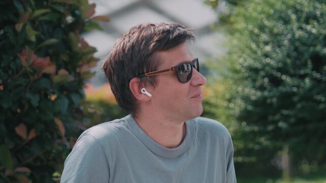 Music listening with wireless earbuds, relaxed man enjoying calm moment outdoors in city park, personal audio comfort and positive urban lifestyle.