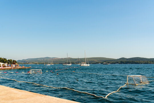 Tivat, Montenegro - 01 August 2025: View of a water polo court set up in the Adriatic Sea with sailboats and coastal hills in the background under a clear blue sky.