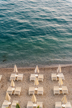 Tivat, Montenegro - 01 August 2025: View of rows of sun loungers and parasols on a pebble beach along the clear blue waters of the Adriatic Sea in Tivat, Montenegro.