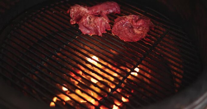 A man puts pieces of raw meat on the grill of a round grill, hot coals under the grill, and an egg-shaped grill.