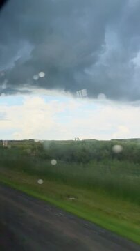 Dramatic storm clouds over green fields with raindrops on window