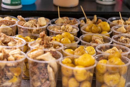 Close-up view of clear plastic cups filled with fried pork rind and Creole yellow potatoes at a street food stand