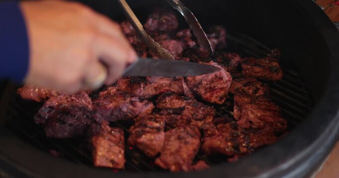 a man checks the readiness of barbecue meat with tongs and a knife on a round grill, cooking a festive dish