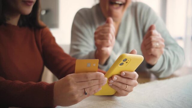 Close-up video of two anonymous women shopping online from home using a credit card and cellphone, highlighting mobile commerce and digital payment.
