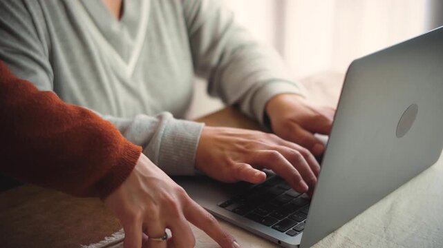 Anonymous young woman's hands teaching her mother how to use a laptop at home, representing digital literacy, family support, technology education, and intergenerational learning.

