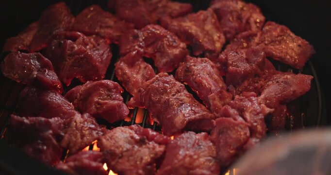 A man puts pieces of raw meat on the grill of a round grill, hot coals under the grill, and an egg-shaped grill.