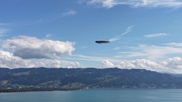 Modern passenger airship flying above Lake Constance with scenic alpine foothills, blue water and dramatic clouds in southern Germany.
