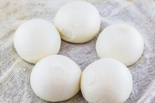 Five white steamed buns are neatly arranged on a textured linen cloth, presented as a close-up still life of plain staple food.