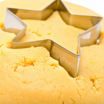 Star shaped metal cutter pressed into yellow dough, creating festive baking pattern with soft crumbly texture and warm kitchen color