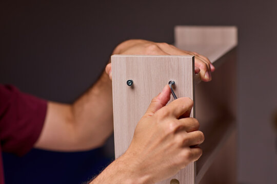 Adult hands cutting stacked corrugated cardboard sheets with utility knife on workbench, close-up of layered edges and precise manual slicing under warm indoor light