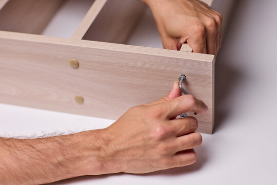 Adult hands cutting stacked corrugated cardboard sheets with utility knife on workbench, close-up of layered edges and precise manual slicing under warm indoor light