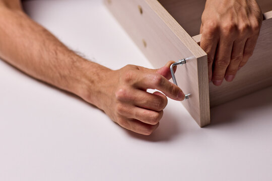 Adult hands cutting stacked corrugated cardboard sheets with utility knife on workbench, close-up of layered edges and precise manual slicing under warm indoor light