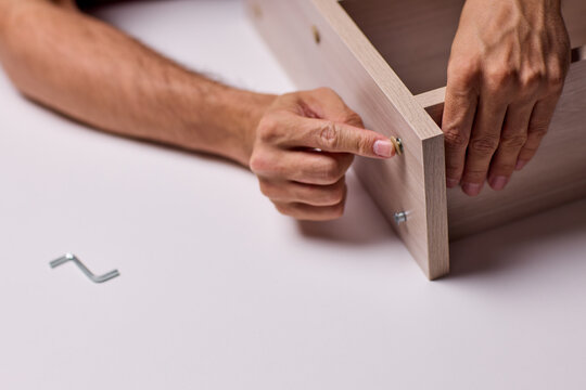 Adult hands cutting stacked corrugated cardboard sheets with utility knife on workbench, close-up of layered edges and precise manual slicing under warm indoor light