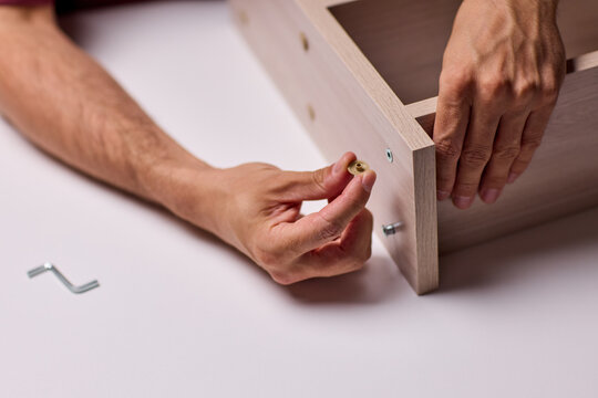Adult hands cutting stacked corrugated cardboard sheets with utility knife on workbench, close-up of layered edges and precise manual slicing under warm indoor light