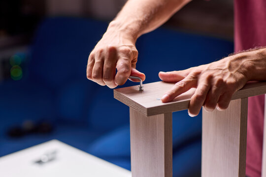 Adult hands cutting stacked corrugated cardboard sheets with utility knife on workbench, close-up of layered edges and precise manual slicing under warm indoor light