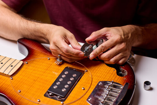 Hands installing humbucker pickup into electric guitar body on workbench in warm workshop light with tools nearby