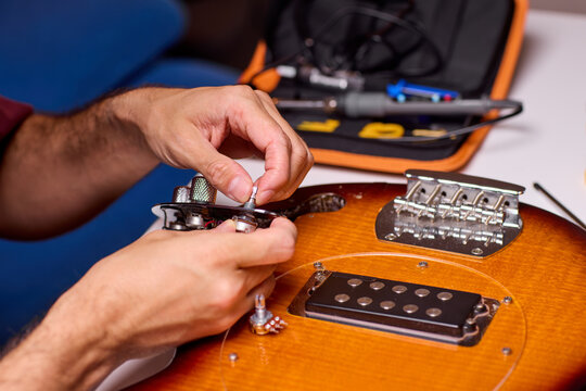 Hands installing humbucker pickup into electric guitar body on workbench in warm workshop light with tools nearby