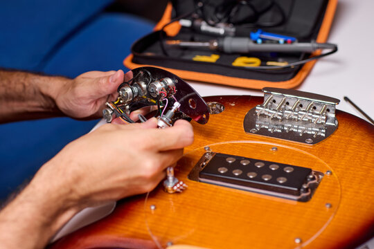Hands installing humbucker pickup into electric guitar body on workbench in warm workshop light with tools nearby