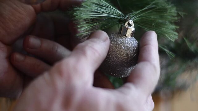 Close up of hand placing silver ball on Christmas tree branch