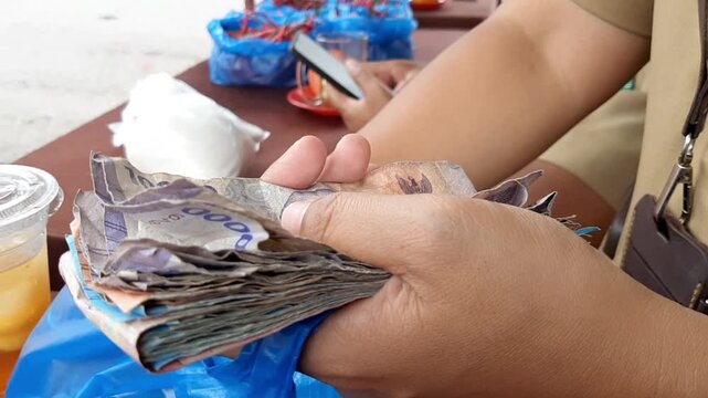 Close-up of Asian hands counting Indonesian rupiah banknotes at a desk