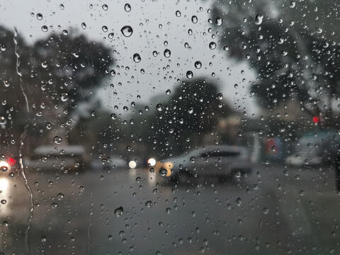 Raindrops Covered Glass Window with Blurred Traffic and Trees in Background on Rainy Day