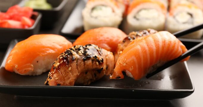 Woman taking delicious nigiri sushi with chopsticks from plate at grey table, closeup