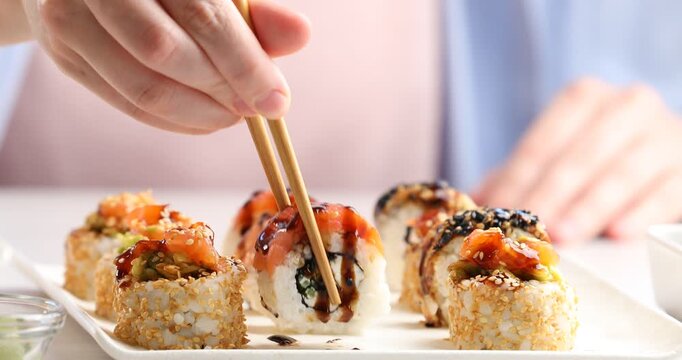 Woman taking tasty sushi roll with chopsticks at white table, closeup