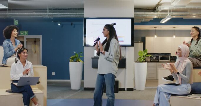 Indian woman presenter stepping forward, speaking into mic at office, sharing charts on screen
