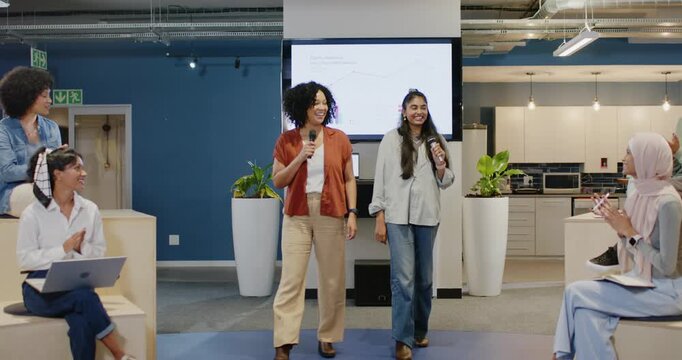 Diverse coworkers walking in office holding mics after team clapping, presenting chart on screen