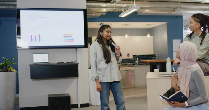 South Asian woman with mic presenting charts hijab peer noting while curly woman joining