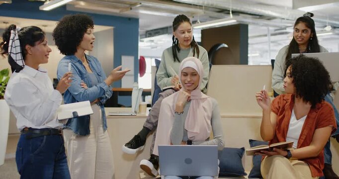 Female team meeting in open office, left woman talking, pointing hijab woman replying with laptop