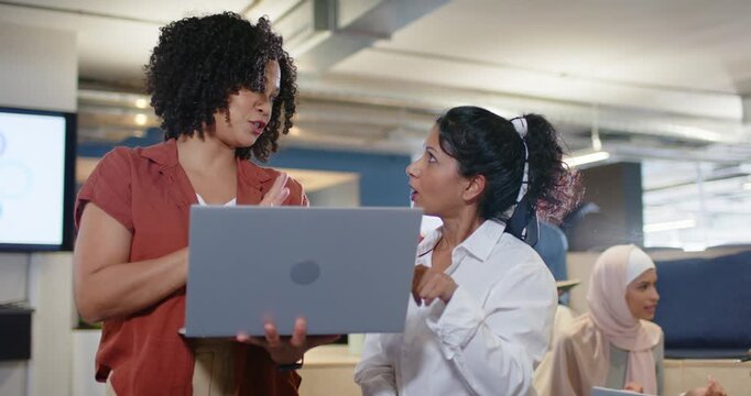 Diverse female coworkers discussing laptop in office, shorter woman's question clarifying details