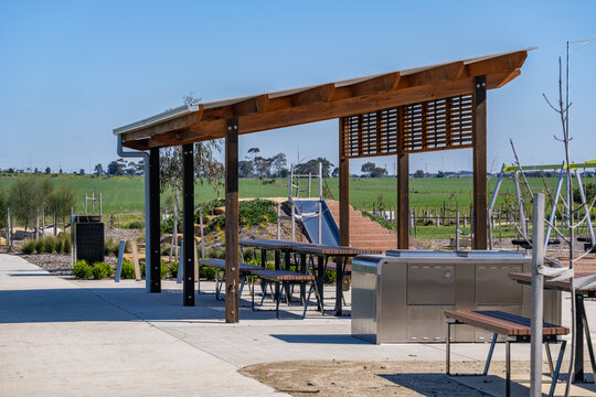 Modern covered picnic shelter with wooden pergola, barbecue facilities, seating, and playground equipment in a new residential housing estate in Truganina, Melbourne, Victoria, Australia.