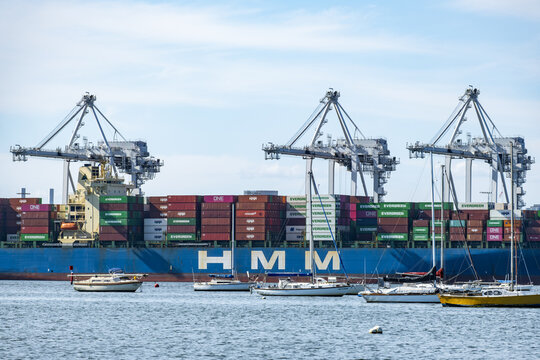 Massive HMM container ship docked under giant gantry cranes at the Port of Melbourne shipping terminal near Newport, seen past leisure yachts at the Yarra River mouth in Melbourne, Australia.