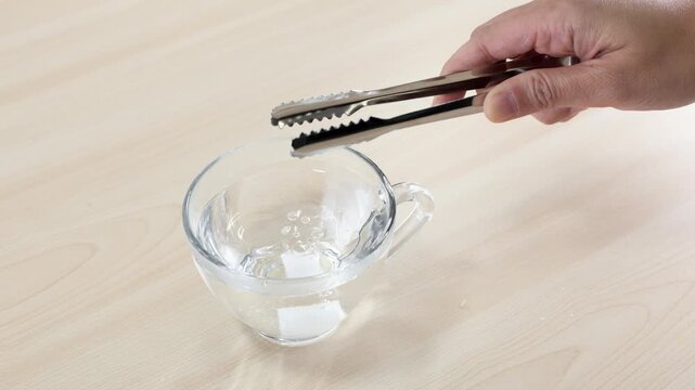 Dropping Sugar Cube into Glass Cup of Water with Tongs