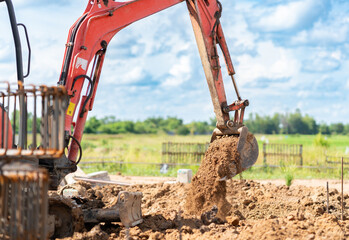 Hydraulic arm of a mini digger scooping and moving brown dirt for ground leveling and foundation work under a bright sky. © Zblaster